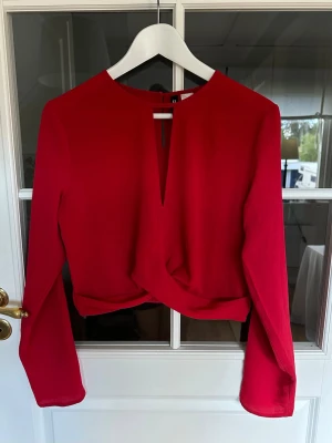 Röd blus - Feminin blus i en intensiv röd nyans. Modellen har långa ärmar, rund halsringning med diskret öppning framtill samt en elegant twistdetalj nedtill som ger ett fint fall och en smickrande silhuett💫
