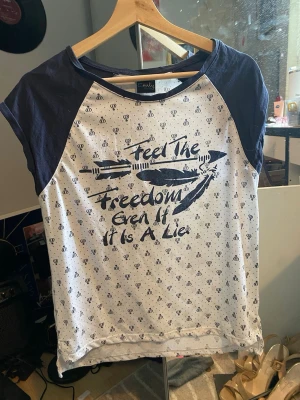 Vit och marinblå t-shirt med tryck - T-shirt från Only i vit med marinblå raglanärmar och tryck fram med texten 'Feel the freedom even if it is a lie'. Små mörkblå symboler över hela tyget och kontrastfärgade detaljer. Perfekt för en avslappnad stil.