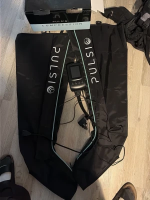 Pulsi kompressionsmaskin med slangar - Elektronisk kompressionsmaskin från Pulsi med tillhörande slangar och kontrollenhet. Svart material med vita och turkosa detaljer. Perfekt för återhämtning och massage av ben. Levereras med originalkartong och strömadapter. Endast använd 3 gånger nypris 4000kr