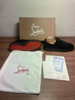 Svarta sneakers från Christian Louboutin - Stilrena svarta sneakers från Christian Louboutin i mocka med klassisk röd sula. Skorna har svarta skosnören, diskret branding och en låg silhuett. Perfekta för dig som vill ha en lyxig och tidlös sneaker med exklusiv känsla. Använda en gång. 