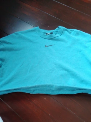 Turkos cropped sweattröja från Nike - Säljer en turkos cropped sweattröja från Nike med klassisk Swoosh-logga broderad på bröstet. Tröjan har rund halsringning och är gjord i mjukt bomullsmaterial. Perfekt för en avslappnad och sportig look