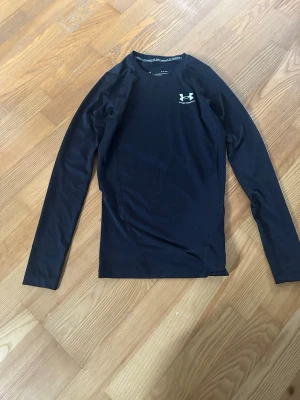 Svart långärmad träningströja UA - Svart långärmad träningströja från Under Armour med logga på bröstet. Tillverkad i ett stretchigt funktionsmaterial som andas, perfekt för intensiva träningspass eller löpning. Slim fit-modell som sitter tajt mot kroppen. Skulle säga att den är s/xs, använt den typ 3 gånger bara. 