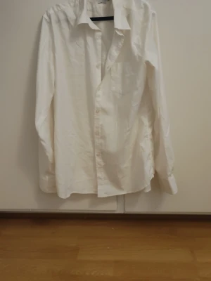 Vit klassisk skjorta i bomull - Klassisk vit skjorta med lång ärm och knappar framtill. Använts nån enstaka gång. Storlek L och är slim fit. Skjortan har en bröstficka och normal passform. Tillverkad i mjuk bomull, perfekt för en clean och stilren look.