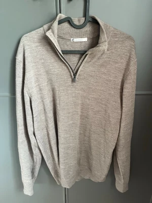 Beige stickad halvzip från Conrad C - Stickad beige tröja från Conrad C med halvzip och hög krage. Tröjan har en mjuk och tunn stickning, långa ärmar och ribbade muddar. Perfekt för lager på lager och enkel att matcha med olika outfits. Kan gå ner i pris vid snabb affär