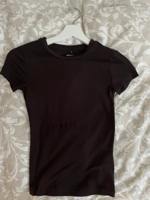 Mörkbrun t-shirt från Gina Tricot - En enkel och stilren mörkbrun t-shirt från Gina Tricot. Modellen har rund halsringning och korta ärmar. 
