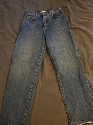 Blå raka jeans i klassisk modell - Säljer ett par blå jeans med rak passform och hög midja. Bälteshällor och stängs med dragkedja och knapp. Tillverkade i kraftigt denimtyg som ger en tidlös look. Perfekta till sneakers eller boots.