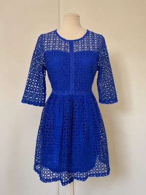 Blå virkad klänning M/L – crochet dress i koboltblått - Supersnygg blå klänning med trekvartsärmar och rund hals. Klänningen har ett genombrutet mönster och markerad midja som ger en feminin siluett. Perfekt för dig som vill sticka ut med färg och detaljer. Dragkedja bak för enkel påklädning.