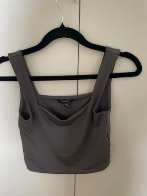 Mörkgrå crop top från Amisu - Snygg mörkgrå crop top från Amisu med breda axelband och draperad urringning. Tillverkad i ett mjukt, stretchigt sportmaterial som sitter skönt på kroppen. Perfekt att matcha med höga jeans eller kjol.