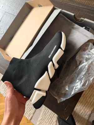 Balenciaga Speed Trainer svarta sneakers - Säljer ett par Balenciaga Speed Trainer sneakers i svart med vit chunky sula. Skorna har en strumpliknande form och är tillverkade i stretchig syntet med Balenciaga-logga på sidan. Perfekta för dig som gillar en modern och clean look.