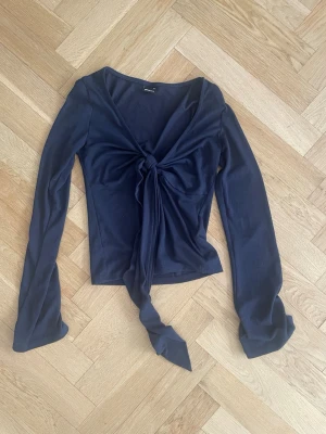 Mörkblå långärmad topp med knyt - Trendig mörkblå långärmad topp med snygg knytning framtill och djup v-ringning. Tillverkad i mjukt och stretchigt material som sitter skönt på kroppen. Perfekt för dig som vill ha en stilren men ändå unik look.