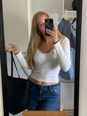 Vit långärmad topp - Säljer en vit topp med lång ärm och v-ringad urringning. Toppen har en figurnära passform och är tillverkad i ett mjukt, stretchigt material som känns bekvämt mot huden. Perfekt att styla med jeans eller kjol för en trendig look.