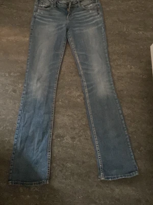 Vintage 2000s Blå bootcutjeans från Silver jeans - Snygga blå vintage bootcutjeans från silverjeans med slitningar och broderade bakfickor. Jeansen har klassisk femficksdesign, låg midja och detaljerade sömmar. Perfekta för dig som gillar en avslappnad men trendig stil. otroligt långa jeans passar för dig som är 170+ är själv 173 och det släpar lite till och med. passar både tjejer och killar 
