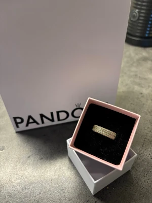 Guldfärgad ring från Pandora stl 56  - Snygg guldfärgad ring från Pandora med glittrande stenar i flera rader runt hela ringen. Kommer i original ask. Perfekt accessoar för att lyfta din stil.