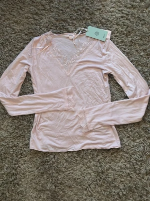 Ljusrosa topp från gina tricot  - Säljer en ljusrosa långärmad topp från Gina Tricot med v-ringning och fina spetsdetaljer vid halsringning och ärmslut. Mjuk och stretchig material, aldrig använd med lappen kvar, nypris 230, mitt pris 150❤️
