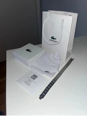 Lacoste silverfärgat armband - Snyggt armband från Lacoste i silverfärgad metall med ett stilrent rutmönster. Kommer med originalpåse, ask och presentpåse från Lacoste. Perfekt accessoar för dig som gillar klassisk och modern design.