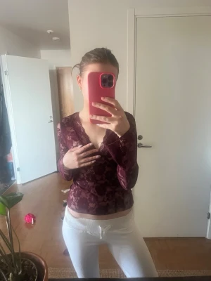 Vinröd spetsblus med v-ringning - Vinröd blus från Gina Tricot i genombruten spets med blommigt mönster. Djup v-ringning och trekvartsärm. 