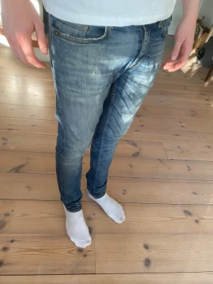 Blå slim fit jeans från tiger of Sweden  - Säljer ett par blå slim fit jeans från tiger of Sweden med klassisk femficksdesign och dragkedjegylf. Jeansen har en lätt tvätt och sen lite svart tyg i de blåa som ses på bilden men tänks inte på vid andvändning