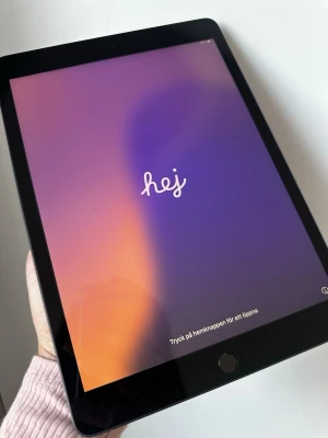 Apple iPad surfplatta 128 GB 10.2” iPad 7 - Snygg svart iPad från Apple med stor skärm och tunn design. Baksidan är i metall med Apple-loggan och texten 'iPad'. Perfekt för surf, spel och streaming. Klassisk rund hemknapp på framsidan och stilren look.
