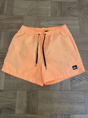 Quiksilver persikofärgade badbyxor - Snygga persikofärgade badbyxor från Quiksilver med svart dragsko och elastisk midja. Klassisk modell med sidofickor och en bakficka. Bra skick!