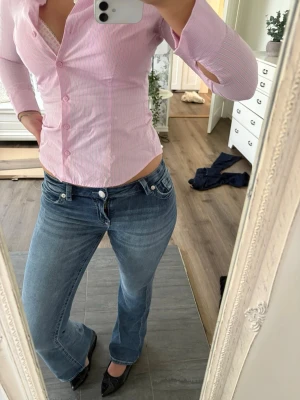 Blå bootcut jeans med låg midja - Säljer ett par klassiska blå bootcut jeans med låg midja och fem fickor. Jeansen har en snygg tvätt och subtila slitningar för en avslappnad look. Perfekta för dig som gillar en tidlös och trendig stil.