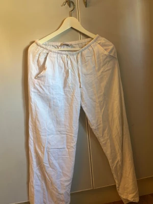 Vita linnebyxor med resårmidja - Säljer ett par vita linnebyxor med avslappnad passform och resår i midjan samt dragsko. Byxorna har raka ben och sidofickor, perfekta för en chill och luftig stil. Materialet är linne vilket gör dem svala och bekväma.
