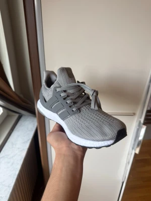 Grå Adidas Ultraboost sneakers - Snygga grå Adidas Ultraboost sneakers med stickad ovandel och klassisk Boost-sula i vitt. Skon har gråa snören, plastdetaljer på sidorna och svart yttersula. Perfekt för dig som gillar sportig och stilren look.