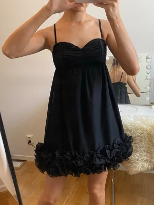 Svart kort klänning från H&M - Supersöt svart kort klänning från H&M med smala axelband och hjärtformad urringning. Klänningen har volangdetaljer längs fållen och en lätt utsvängd passform. Perfekt för dig som gillar en feminin och trendig look.