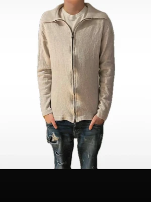 J.Lindeberg cardigan  - Snygg beige cardigan från J.Lindeberg med hel dragkedja framtill och hög krage. Cardiganen är tillverkad i ett mjukt tyg och har en stilren, minimalistisk design utan huva. Perfekt för dig som gillar en clean look. Krymt i tvätten så passar en som är runt 160cm lång!