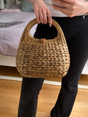 Flätad handväska i naturmaterial - Snygg handväska i flätat naturmaterial med rundade handtag och en dekorativ knäppning upptill. Väskan har en mjuk, rundad form och ger en bohemisk känsla. Perfekt för dig som gillar en unik accessoar med naturlig look. Helt ny och aldrig använd⭐️