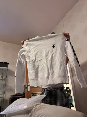 Off-White sweatshirt med tryck - Säljer en vit sweatshirt från Off-White med svart logga framtill och stora svarta pilar på ryggen. Ärmarna har svarta ränder och tryck. Tröjan har rund hals och är gjord i mjukt bomullsmaterial. Kvitto finns självklart Stl S men lite stor i stl. Köpt gör 3500.