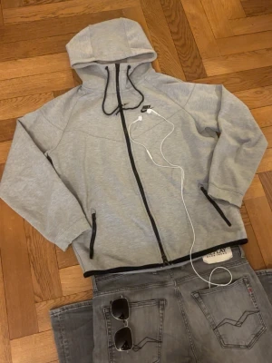 Grå Nike hoodie med zip-up - Grym kvalité, inga defekter. Storlek är M, passformen sitter bra. Men Kolla måtten så de passar:)                                                                   Mått -|-  Axelmått: 55 cm  Längd: 64 cm  Bröst: 57 cm  Arm: 52 cm.                                        Leverans sker dagen efter, men har du nån fråga är det bara att skriva :)