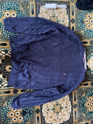 Mörkblå stickad tröja från Fila - Säljer en mörkblå stickad tröja från Fila med diskret fiskbensmönster och liten broderad logga på bröstet. Tröjan har rund halsringning och ribbade muddar vid ärmslut och nederkant. Perfekt för dig som gillar klassisk och stilren design.