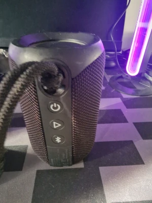 Ultimate Ears trådlös högtalare svart - Snygg och robust trådlös högtalare från Ultimate Ears i svart. Cylindrisk form med grovt textilmaterial runt om, stora volymknappar och praktisk bärrem. Perfekt för att ta med sig musiken överallt och enkel att koppla via Bluetooth.