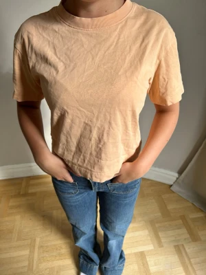 Persikofärgad croppad t-shirt💖💖 - En enkel och stilren persikofärgad t-shirt med croppad passform och rund halsringning. T-shirten har korta ärmar och är tillverkad i mjuk bomull, perfekt för en avslappnad look.