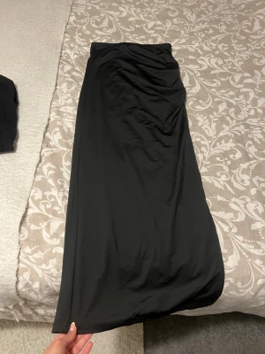 Svart långkjol från SHEIN - Svart långkjol från SHEIN i enkel och stilren design. Kjolen har rak passform och är tillverkad i ett mjukt och lätt material som ger en snygg siluett. Perfekt att styla med crop tops eller stickade tröjor.
