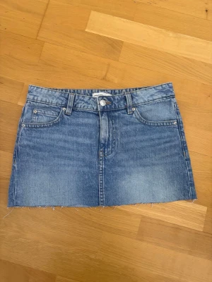 Mellanblå jeanskjol - Snygg blå jeanskjol från Gina Tricot. Den är lågmidjad, perfekt längd, en klippt kant och bakfickor med knapp. Aldrig använd 