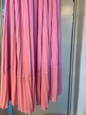 Lång rosa kjol med volang stlk 38 - Säljer en lång, luftig rosa kjol med volangdetaljer. Kjolen har ett flowigt fall  och dragkedja i sidan, och är perfekt för dig som gillar en feminin och trendig stil. Passar snyggt till både sneakers och sandaler. Från Hm stlk 38