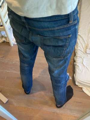Nudie jeans slim - Storlek W30 L34. Snygga blå jeans med raka ben och stora bakfickor. Jeansen har klassisk femficksdesign och är tillverkade i denim med lätt tvättad look. Perfekta för en avslappnad och trendig stil. Tyvärr defekter i framfickan men inget som syns vid användning.