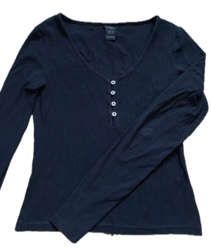 Henley shirt - Säljer en henley shirt, även kallad farfartröja eller knäpptröja, som är svart och i ribbat tyg. Tröjan har pärlemorknappar, och har en u ringning. Den visar inga tecken på användning då den är använd endast ett fåtal gånger.