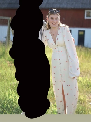 Adoore klänning med blommigt mönster - Superfin vit lång adoore klänning med små röda blommor, djup v-ringning och långa puffärmar. Klänningen har markerad midja, knappar framtill och en slits som ger extra rörelse. Perfekt för sommarens alla tillfällen! (Ända att anmärka på är att en knapp längst ner har försvunnit. Men ingenting som syns elelr stör klänningens funktion!)