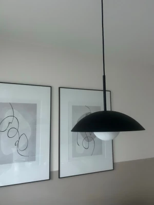 Svart taklampa i modern design från HM - Säljer en stilren svart taklampa med rund, kupad skärm och vit glödlampa. Lampan har minimalistisk och modern form, perfekt för att ge rummet en trendig känsla. Passar bra över matbord eller i vardagsrum.