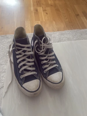 Converse All Star svarta high tops - Klassiska Converse All Star high tops i svart canvas med vita gummisulor och tåhätta. Skorna har vita snören och den ikoniska loggan på sidan. Perfekta för en avslappnad och cool stil.