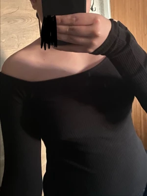 Svart offshoulder ribbad topp - Snygg svart offshoulder topp med ribbad struktur och långa ärmar. Tight passform som framhäver figuren och ger en trendig look. Perfekt att styla med både jeans och kjol.