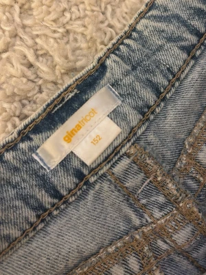 Ljusblå jeans från Gina Tricot - Säljer ett par ljusblå jeans från Gina Tricot i storlek 152. Jeansen har klassisk femficksmodell, synliga sömmar i kontrastfärg och är tillverkade i denim. De har en slit på höger sida som har spruckit en bit upp vilket avslöjar en del av låret .Använda mycket fåtal gånger och ända täcken på användning är slitten.