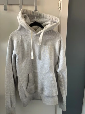 Ljusgrå hoodie från russermerch - Snygg ljusgrå hoodie från Russermerch med stor huva och vita dragsnören. Klassisk känguruficka framtill och ribbade muddar vid ärmslut och nederkant. Perfekt för en avslappnad och sportig stil.