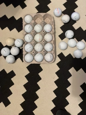 Samling golfbollar i olika märken - Säljer ett gäng vita golfbollar i olika märken och modeller. De är runda och gjorda av hård plast, vissa har tryck med loggor och linjer i olika färger. Perfekt för dig som vill fylla på golfväskan eller träna på rangen.