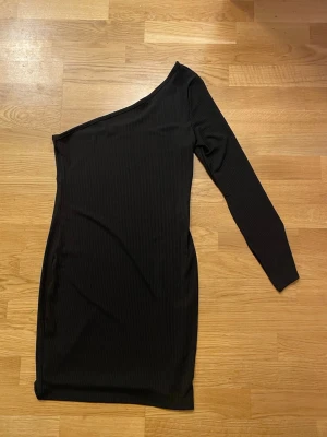 Svart oneshoulder klänning - Snygg svart oneshoulder klänning med lång ärm på ena sidan. Klänningen är ribbad.