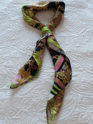 Mönstrad sjal i grönt, svart och rosa - Snygg sjal med färgstarkt mönster i grönt, svart, rosa och guld. Sjalen har kedje- och medaljongmotiv och är tillverkad i ett tunt, glansigt material som känns lyxigt. Perfekt att knyta runt halsen eller i håret för en trendig look.