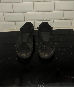 Svarta slip-on sneakers - Säljer ett par helsvarta slip-on sneakers med minimalistisk design. Skorna har en låg siluett och saknar snörning, vilket ger en clean och enkel look. Passar perfekt till streetwear och vardagsoutfits.