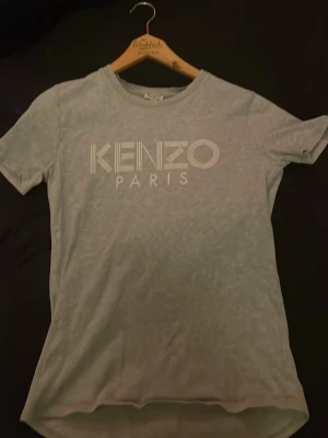 Grå Kenzo Paris t-shirt - Snygg grå t-shirt från Kenzo med klassiskt 'KENZO PARIS'-tryck i vitt på bröstet. T-shirten har rund halsringning och korta ärmar. Perfekt för dig som gillar stilrena och trendiga plagg med designer-touch.
